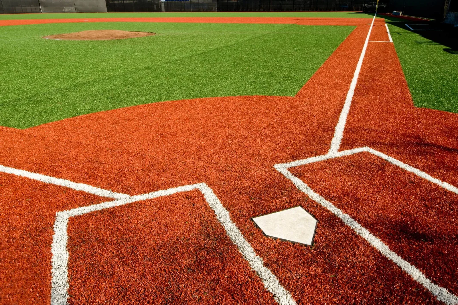 A baseball field in Arizona featuring a close-up view of the home plate area with distinct white lines marking the batter's box and the foul lines. The grassy infield and pitcher's mound are visibly maintained, showing a clear, sunny day perfect for artificial grass installations.